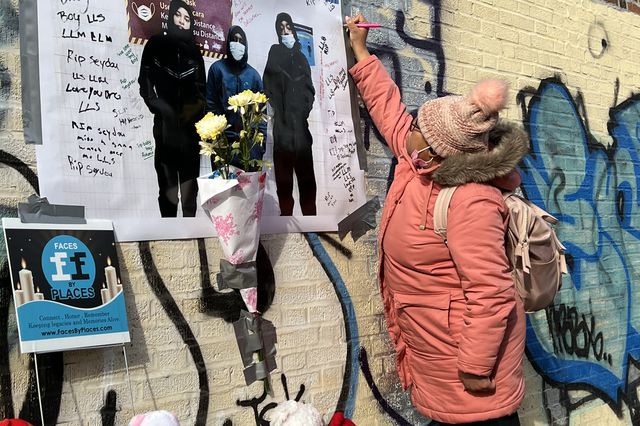 A woman writes a note on a memorial at the site of the Bronx fire